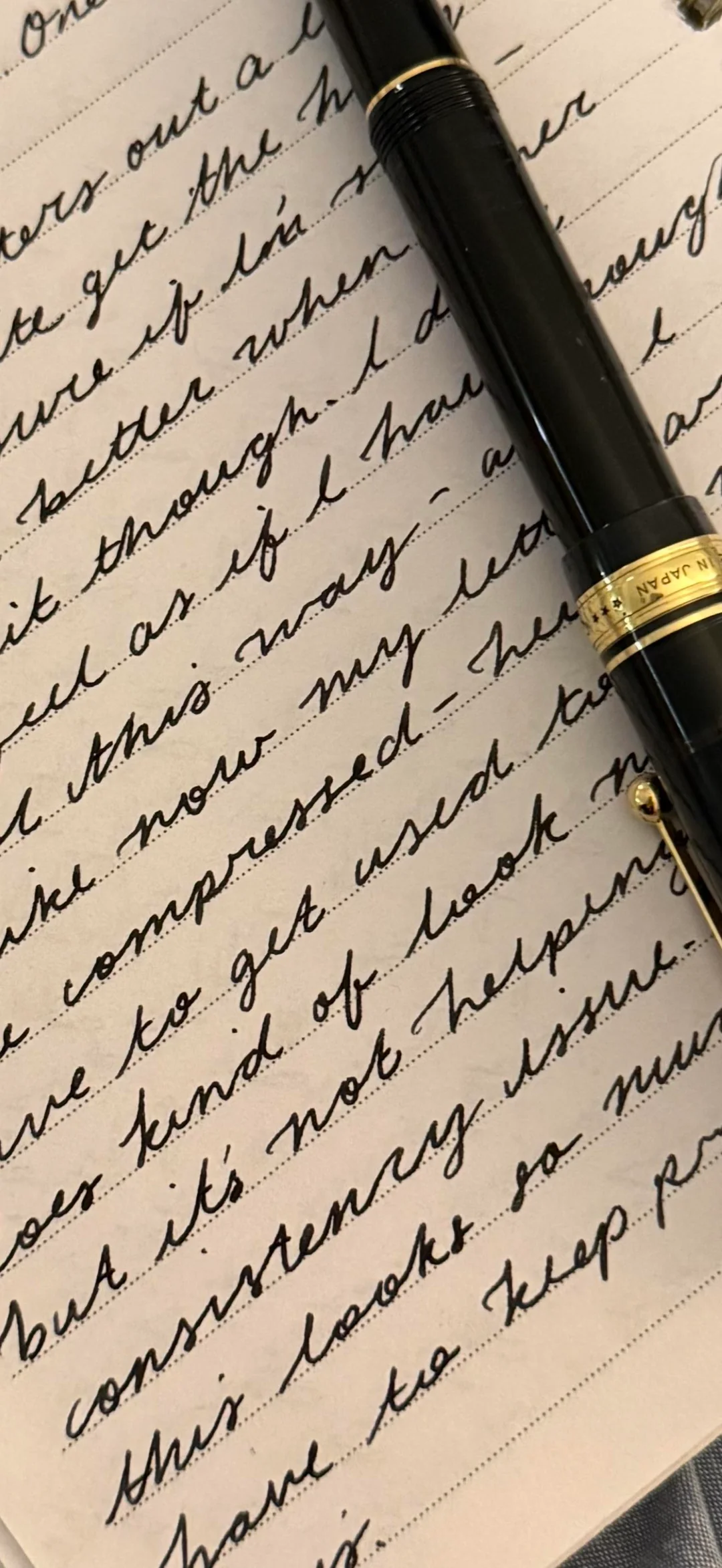 A black and gold fountain pen rests on a page filled with neat, cursive handwriting written in black ink. The pen lies diagonally across the lined paper.