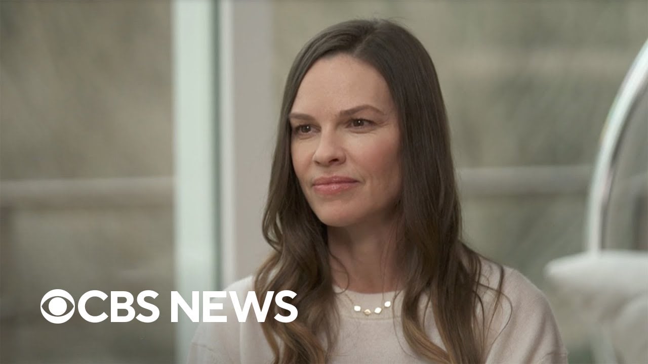 A woman with long brown hair and a light sweater sits indoors, looking slightly to the side. The CBS News logo appears in the lower left corner.