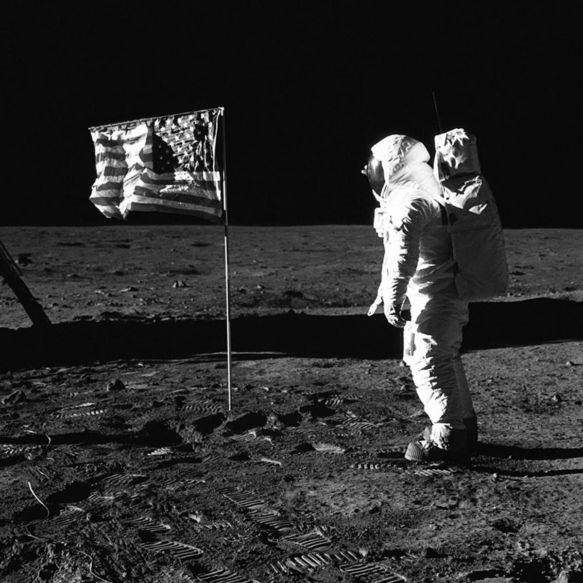 An astronaut in a spacesuit stands on the moon near an American flag, with footprints visible on the lunar surface under a black sky.