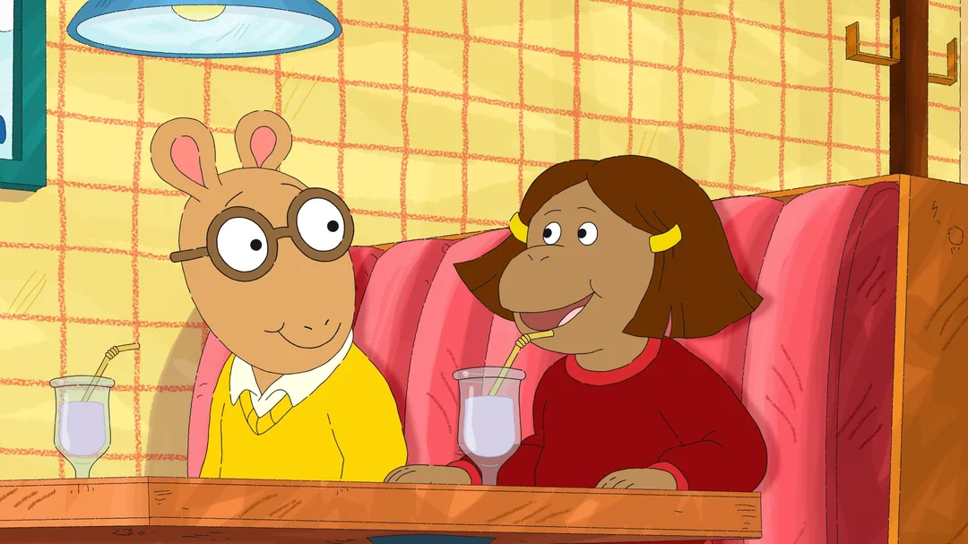 Two animated characters sit in a red booth at a restaurant, each drinking from a glass with a straw. One wears glasses and a yellow sweater, the other has brown hair, a red shirt, and yellow hair clips.