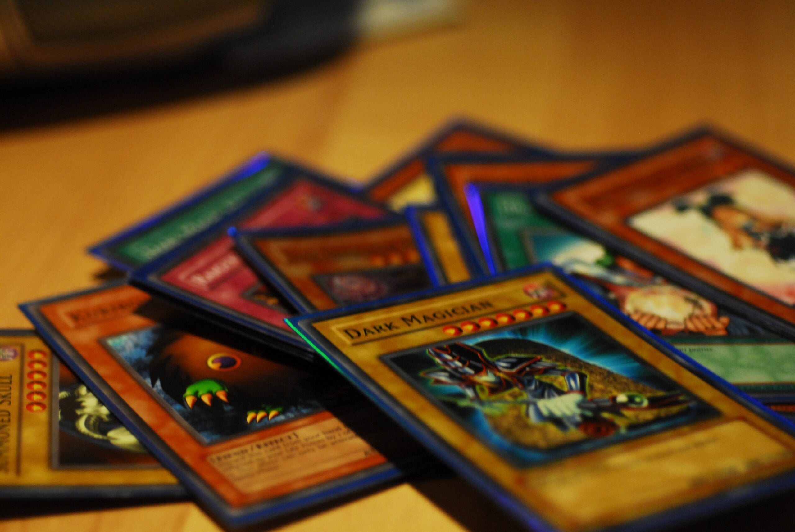 A close-up photo of a scattered pile of Yu-Gi-Oh! trading cards on a wooden surface, with the "Dark Magician" card prominently visible in the foreground.