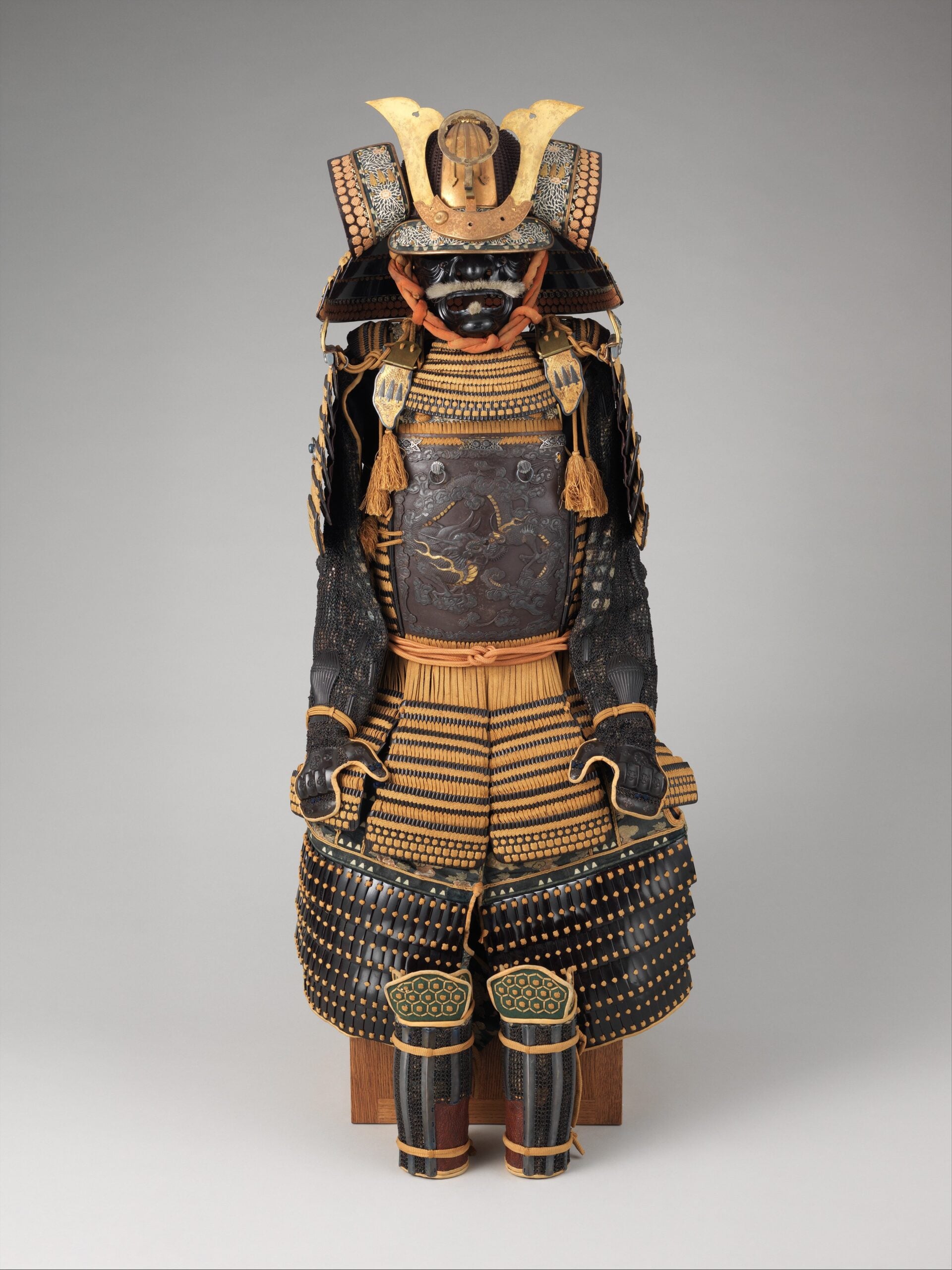 A full suit of traditional Japanese samurai armor with intricate metal and leather detailing, including a helmet with a gold crest, face mask, and protective plating on the chest, arms, and legs.
