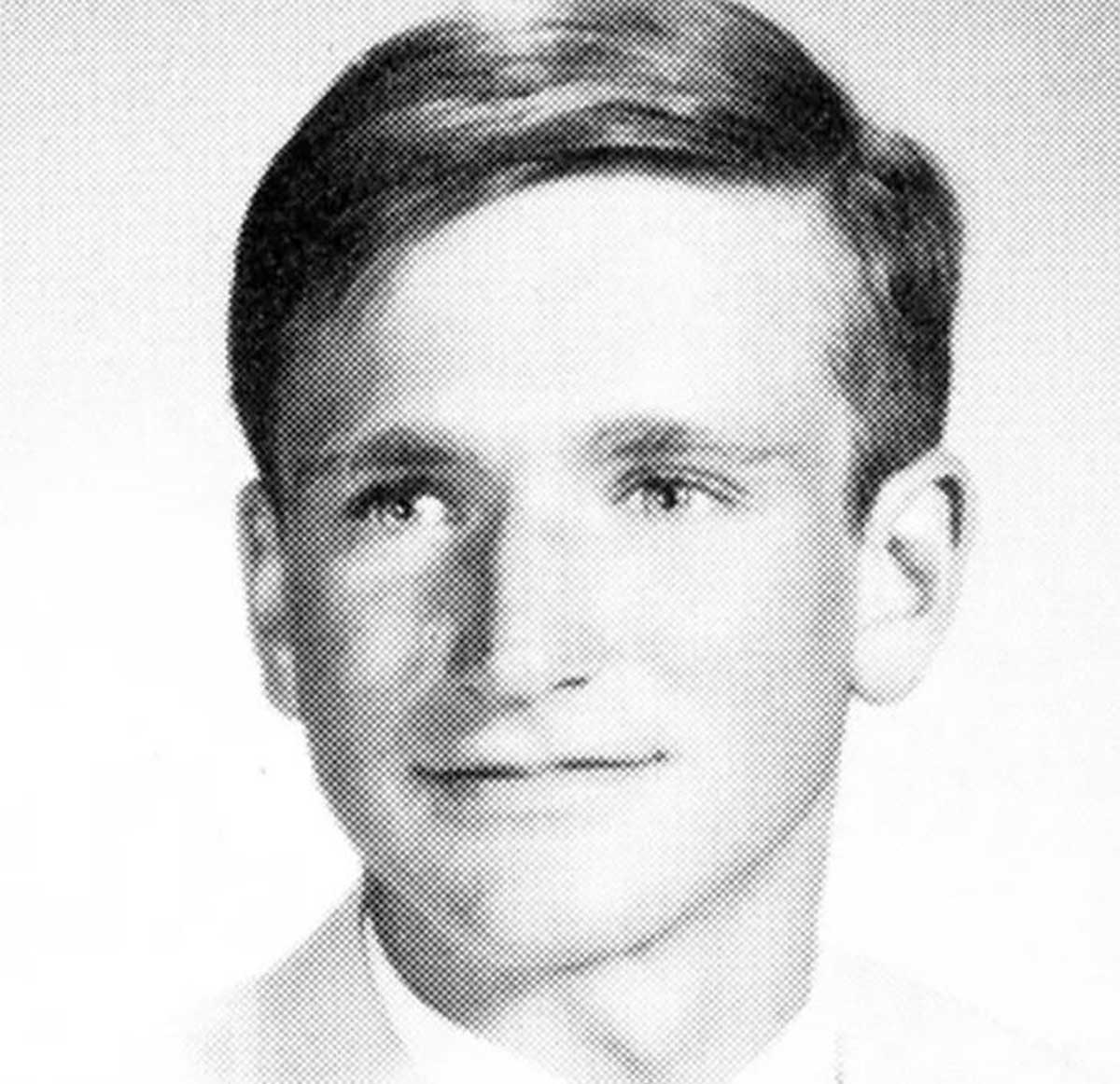 Black-and-white yearbook-style portrait of a young man with short, neatly parted hair, wearing a light-colored jacket, white shirt, and tie, looking slightly to the side and smiling softly.
