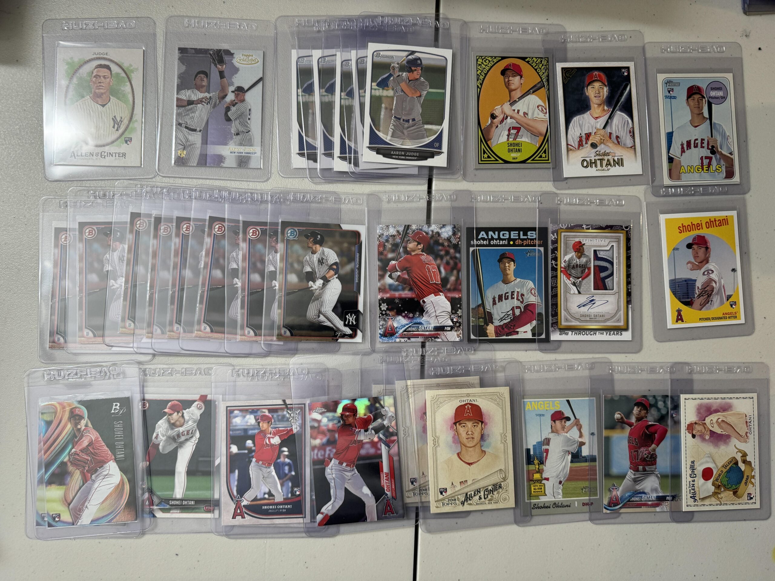 A collection of baseball cards in protective sleeves is arranged on a white surface, featuring multiple Shohei Ohtani cards and a few other MLB players, with a mix of action shots and illustrated designs.