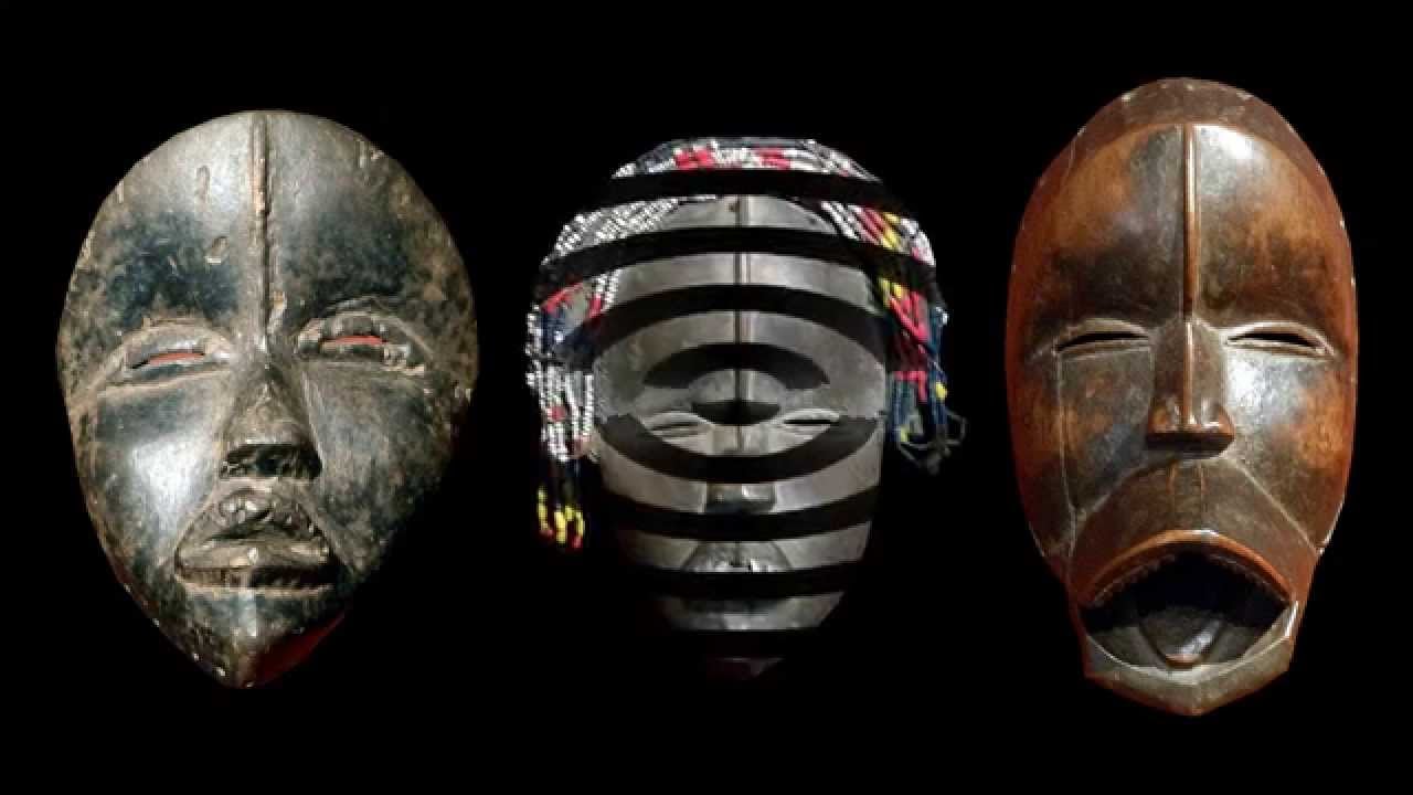 Three traditional African masks are displayed side by side against a black background. Each mask has distinct facial features and designs, with the middle mask decorated with colorful beads and horizontal black bands.