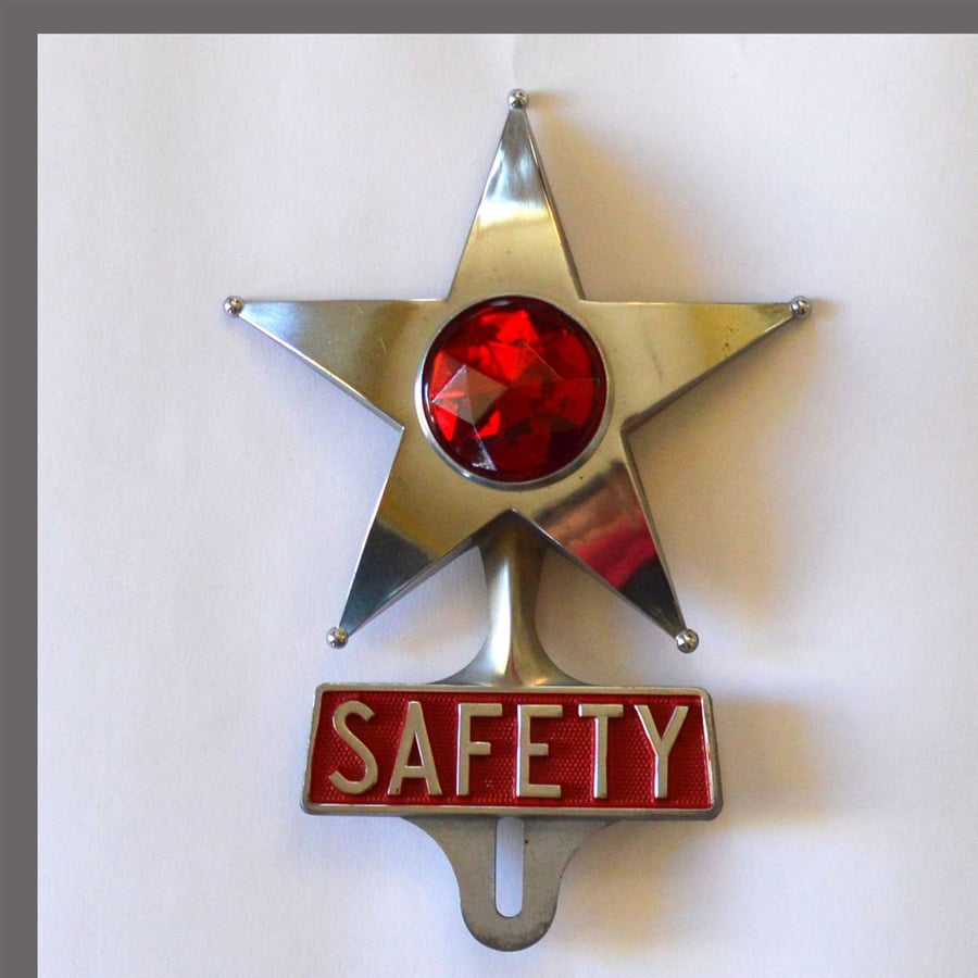 A silver star badge with a large red gem in the center and a red panel at the bottom displaying the word “SAFETY” in white letters, set against a white background.