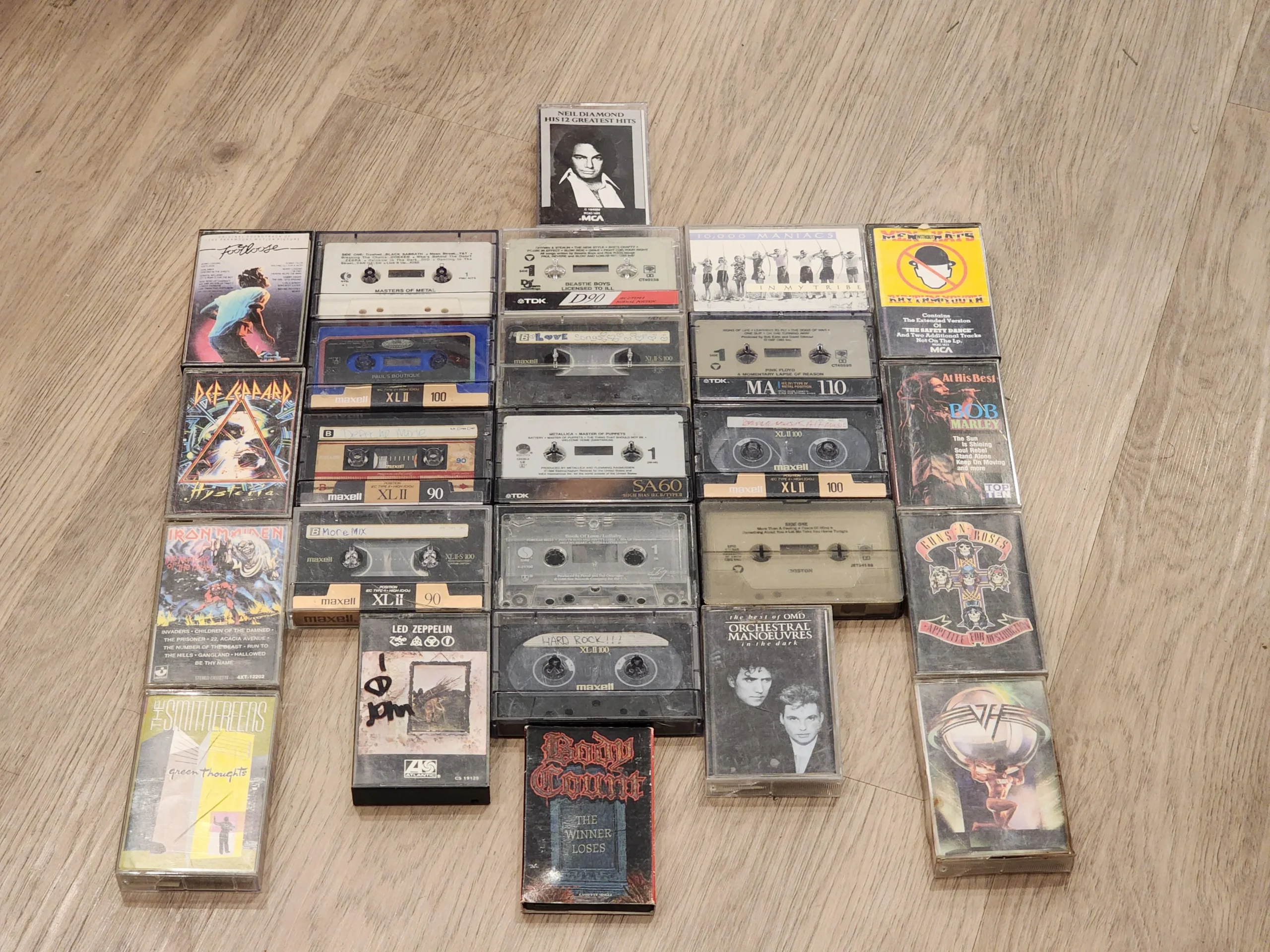 A collection of various audio cassette tapes arranged neatly on a wooden floor, featuring different bands, albums, and labels with colorful and black-and-white covers.