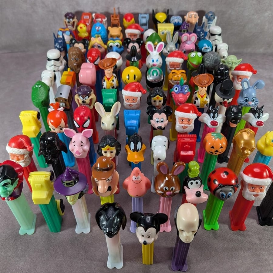 A collection of colorful PEZ dispensers featuring various cartoon and holiday characters arranged in neat rows on a gray surface.