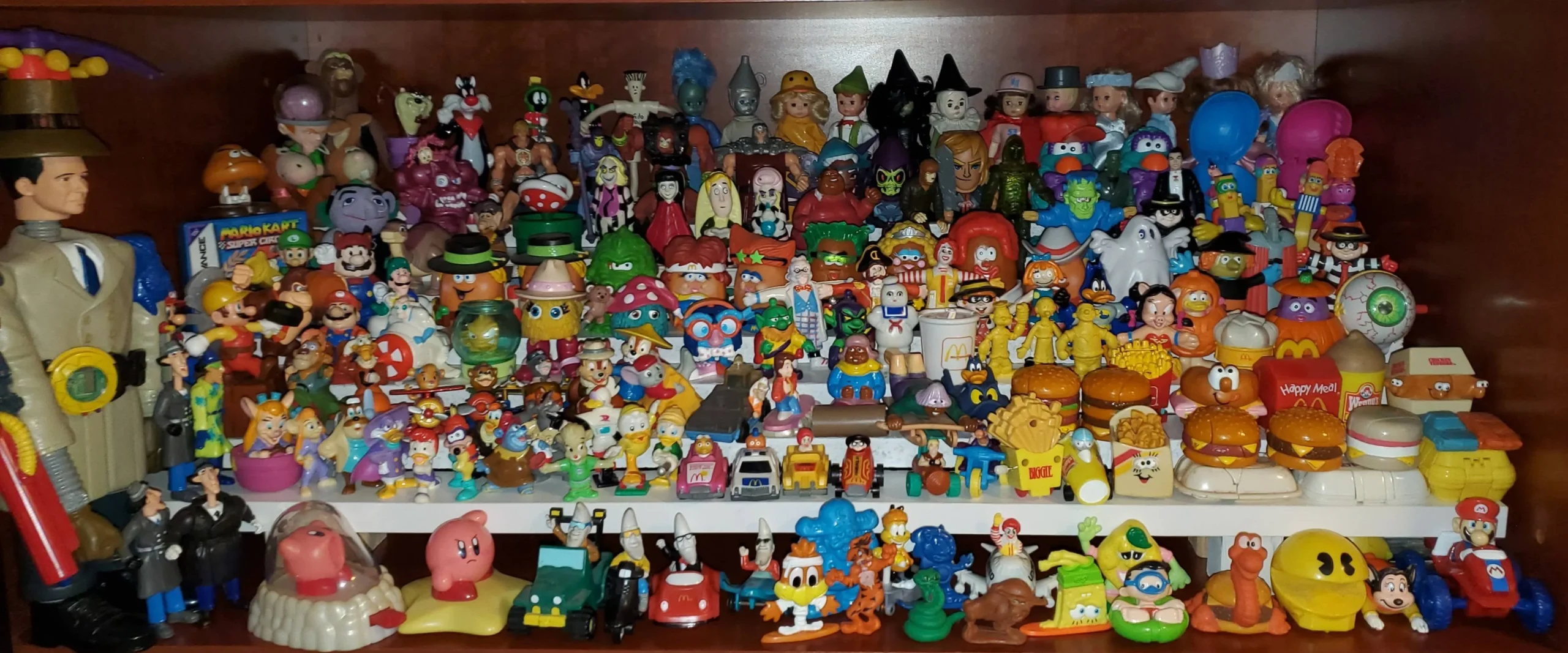 A large collection of colorful fast food and cartoon character toys, including figures from McDonald’s, Burger King, and various animated series, arranged on two shelves with larger toys on the left and smaller figures in front.