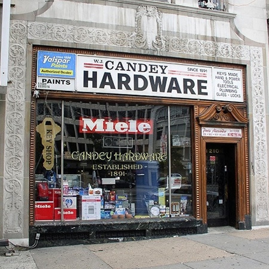 A storefront of Candey Hardware, established in 1891, with a large "HARDWARE" sign, various products displayed in the window, and an ornate building facade. Signs for paint, keys, and other services are visible.