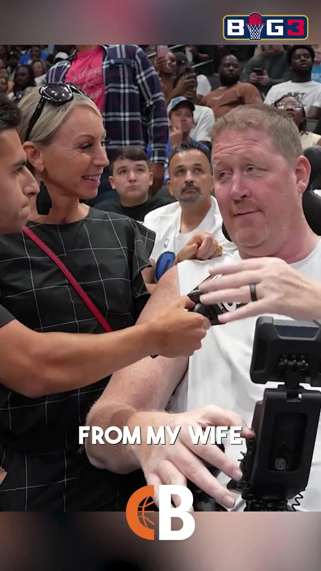 A woman smiles while holding a microphone to a man in a wheelchair at a crowded basketball event. The text "FROM MY WIFE" and a basketball logo appear at the bottom, with the BIG3 logo at the top right.