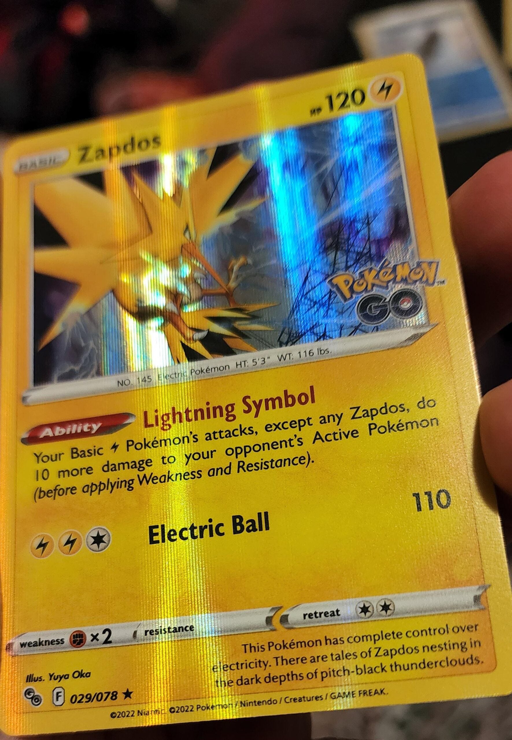 A close-up of a shiny Zapdos Pokémon card from the Pokémon GO series, showing its stats, abilities, and yellow electric-themed artwork, held between someone’s fingers.