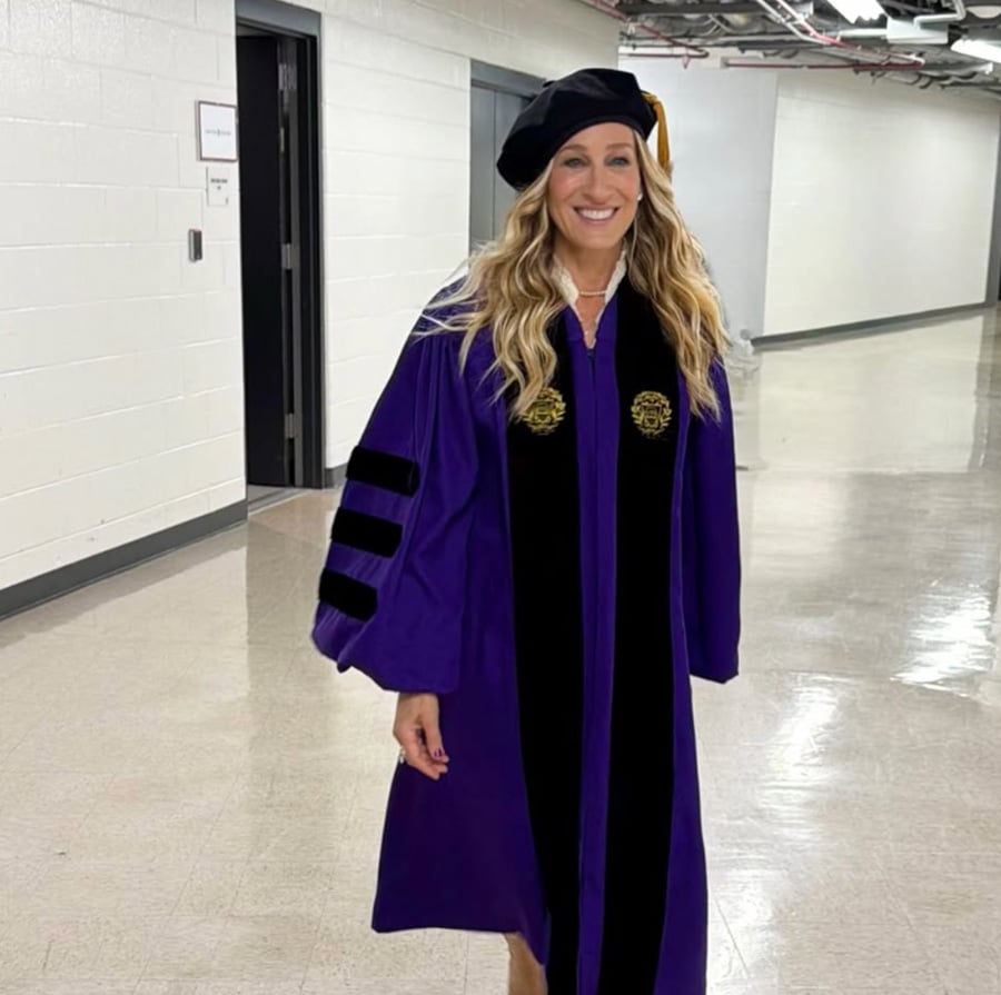 A woman wearing a purple academic gown and black cap smiles while walking down a hallway with light-colored walls and floor.