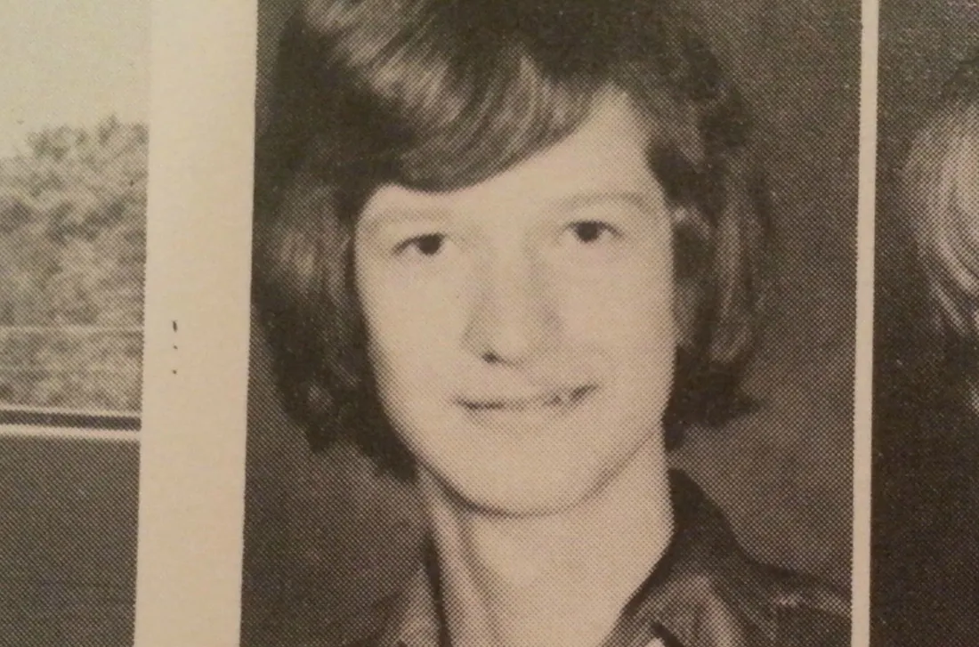 Black-and-white yearbook photo of a young person with short, wavy hair, smiling slightly, and wearing a collared shirt, facing the camera against a plain background.