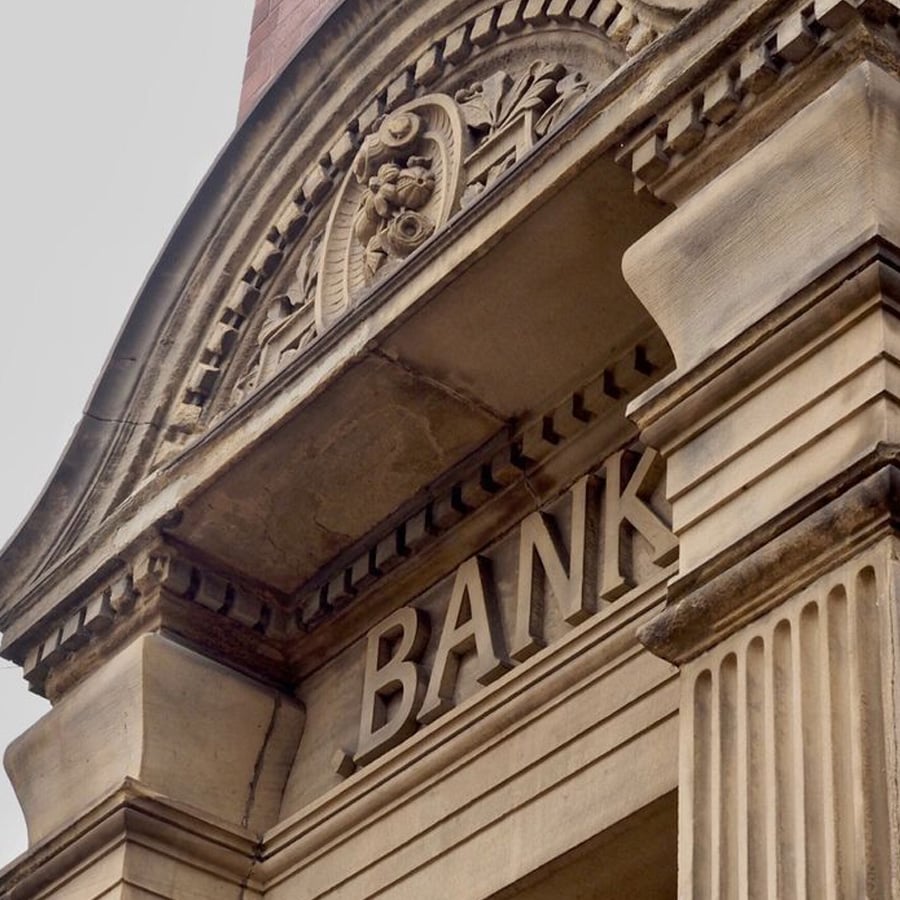 Close-up of a stone building facade featuring the word “BANK” in large letters above the entrance, with ornate architectural details and a decorative carving above.