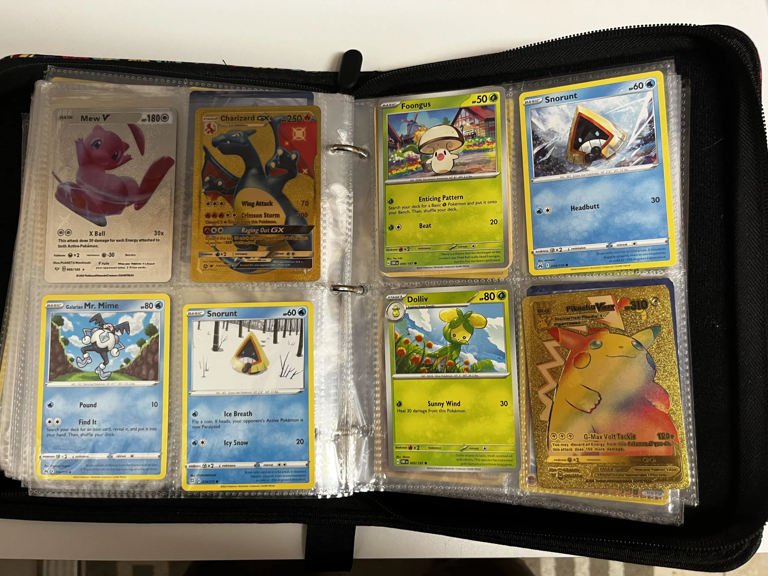 A binder with plastic sleeves contains eight Pokémon cards, including Mew V, Charizard GX, two Snorunt, Foongus, Mr. Mime, Dedenne, and a shiny Pikachu with a festive background.