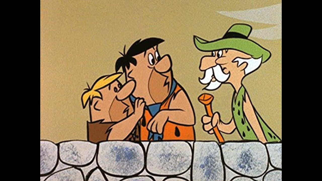 Two cartoon men, one short and blond, one tall with dark hair and an orange vest, stand behind a stone wall talking to an older man in green clothes and a hat with a white mustache and cane.