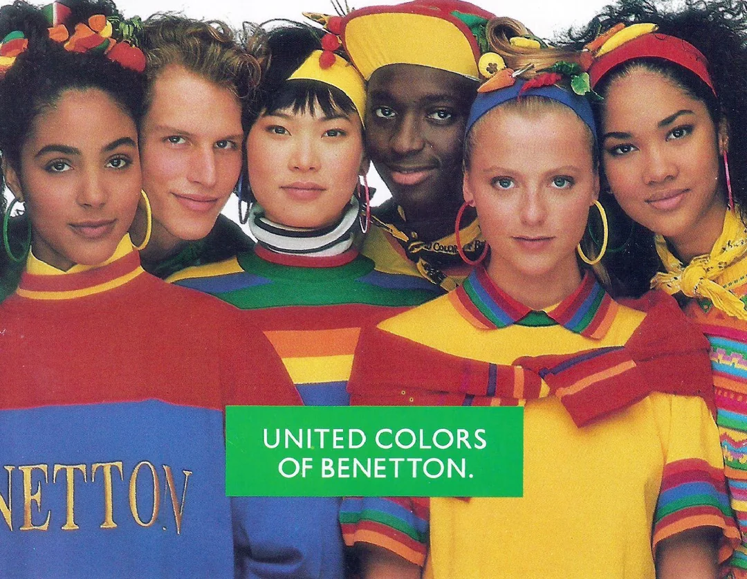 A diverse group of six young people stand close together, wearing colorful, striped Benetton clothing and accessories. A green text box in front reads "United Colors of Benetton.