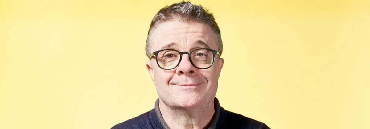 A middle-aged man with short gray hair and glasses smiles softly at the camera, set against a plain yellow background.