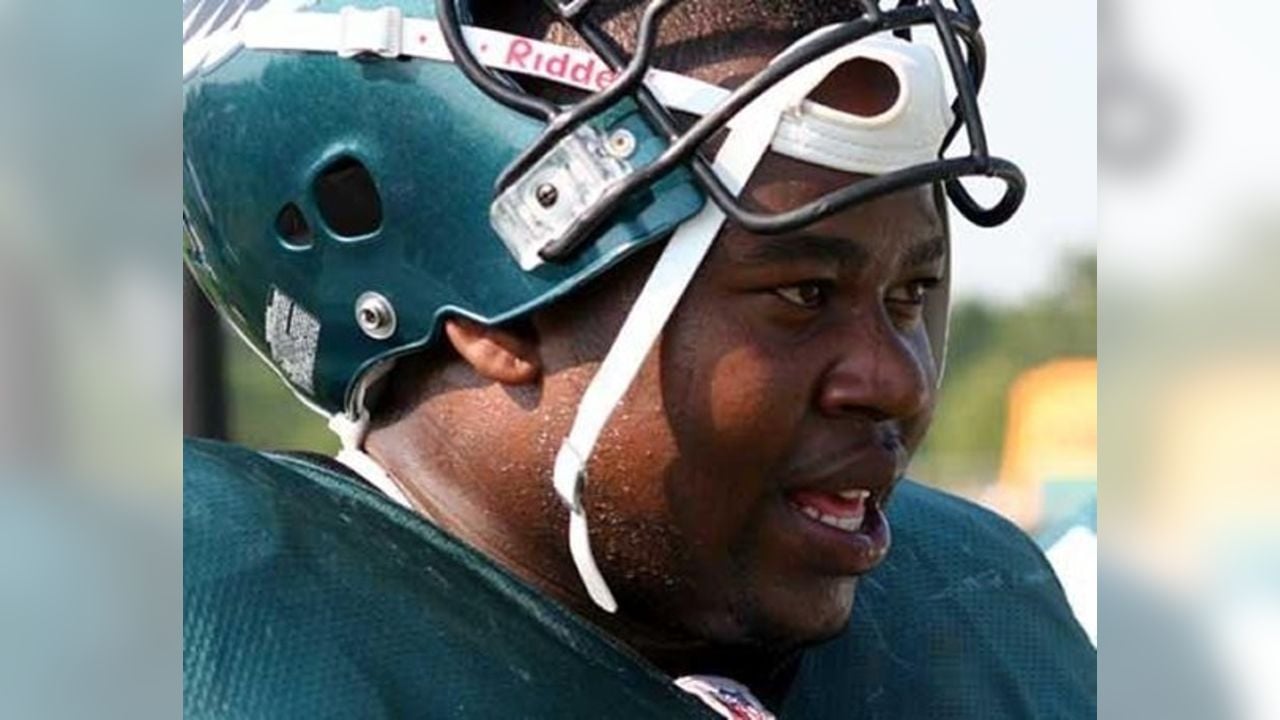 A football player wearing a dark green helmet and jersey is seen close up, sweating and looking focused during what appears to be a game or practice.