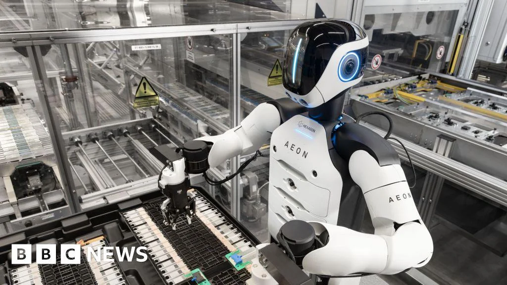 A humanoid robot labeled "AEON" operates machinery in a modern factory setting with glass walls and electronic components in the background. The BBC News logo is visible in the bottom left corner.