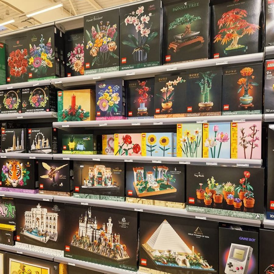 Shelves in a store display various LEGO sets, including botanical flowers, plants, famous landmarks, and architectural models, all in brightly colored boxes.