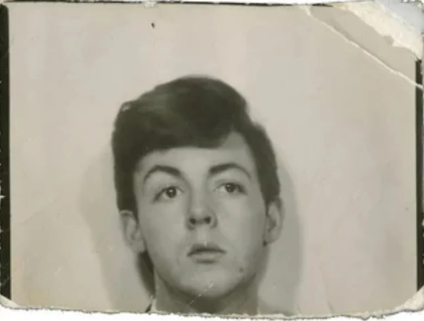 A vintage, slightly damaged black-and-white photo shows a young person with dark hair looking slightly upward. The background is plain, and the photo has creased and worn edges.