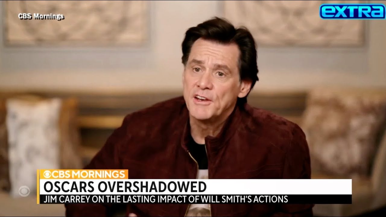 A man with dark hair wearing a maroon jacket speaks during a TV interview. “CBS Mornings” and “extra” logos are visible, with a headline: “OSCARS OVERSHADOWED – Jim Carrey on the lasting impact of Will Smith’s actions.”