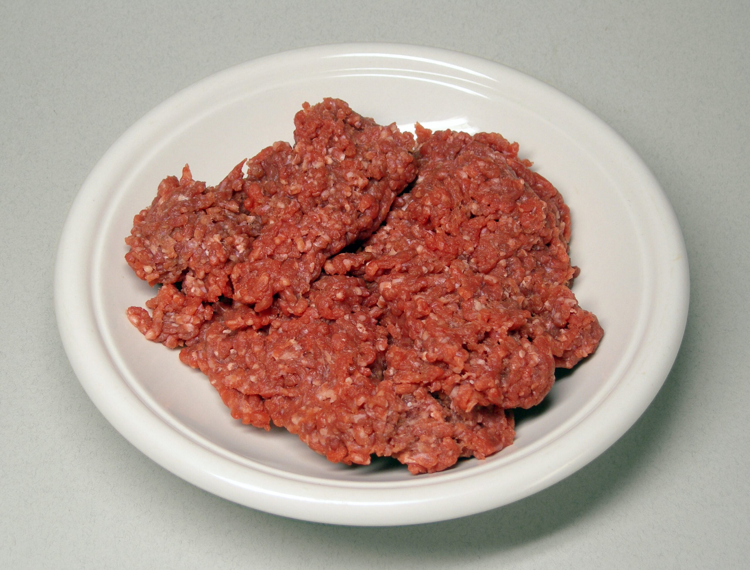 A white plate filled with raw ground beef, placed on a light gray surface.