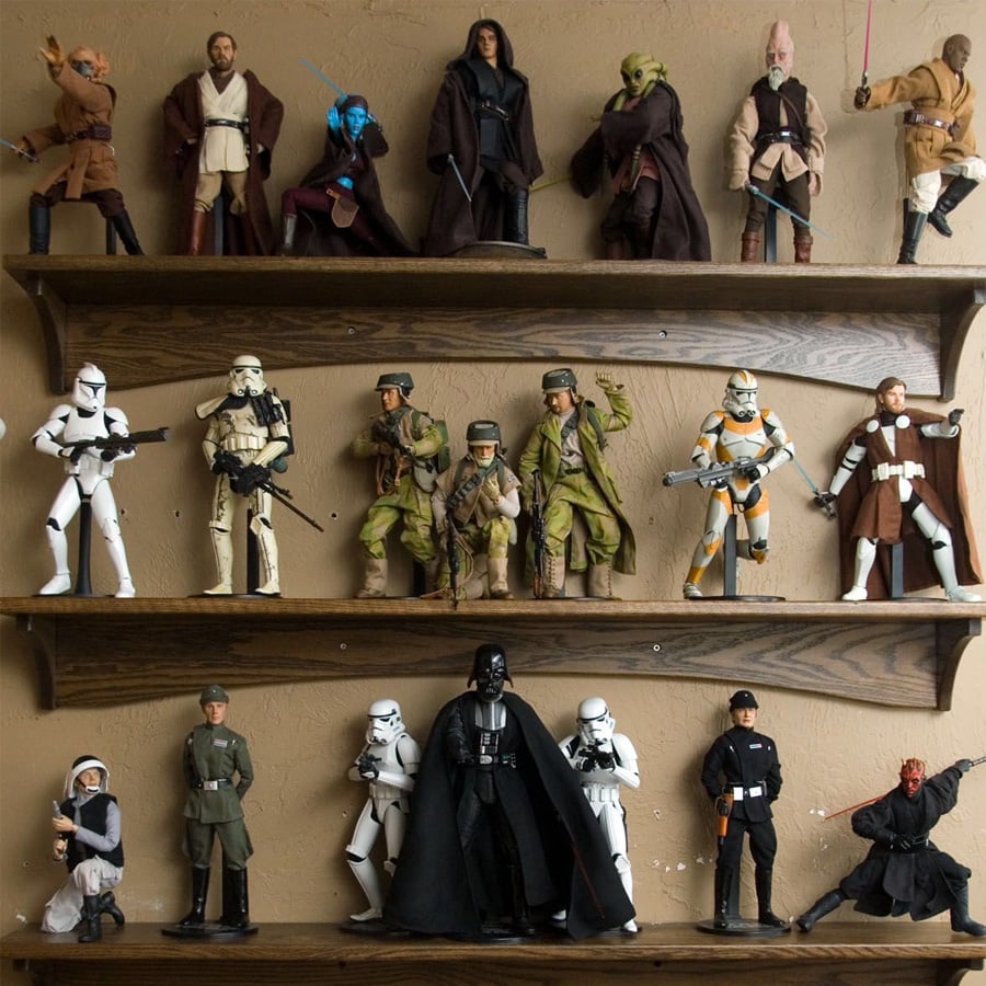 Three wooden shelves display various Star Wars action figures, including Jedi, Sith, clone troopers, stormtroopers, and other characters from the franchise, posed in different stances against a beige wall.