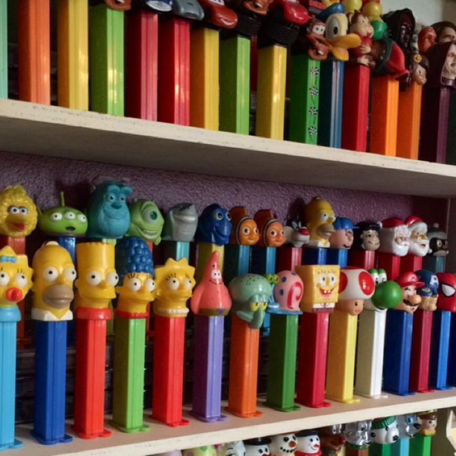 Rows of colorful PEZ dispensers featuring various cartoon and movie characters, including The Simpsons, Toy Story, Finding Nemo, and SpongeBob, displayed on shelves.
