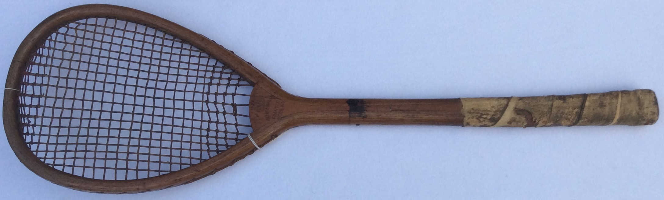 A vintage wooden tennis racket with a worn handle and brown strings, photographed against a plain white background.