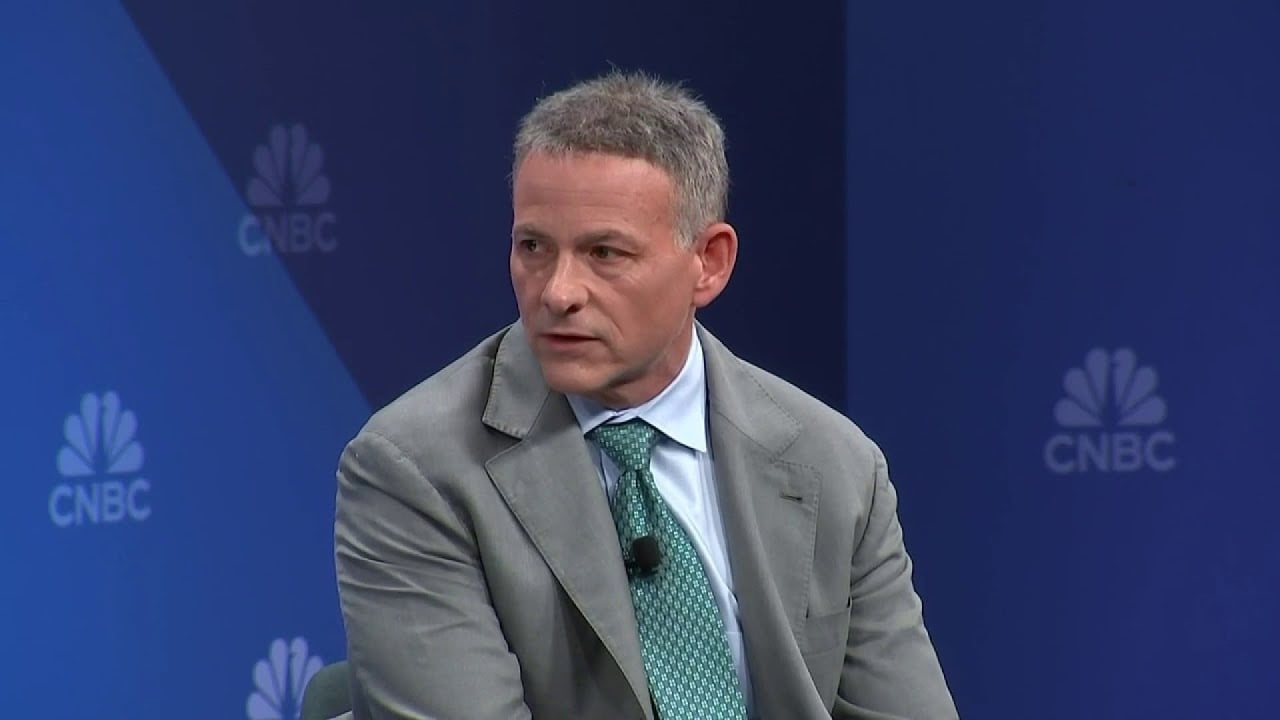 A man in a gray suit and green tie sits and speaks during a CNBC event, with the CNBC logo visible on the blue background behind him.