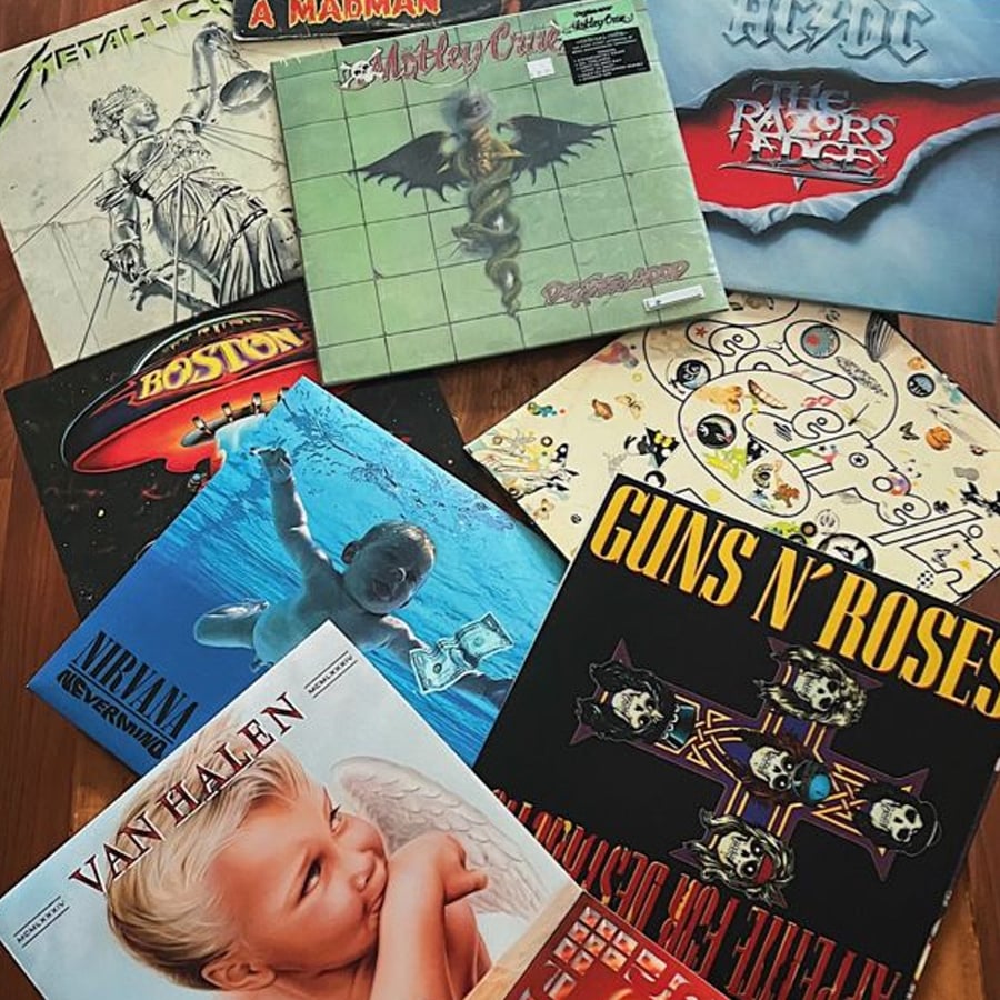 A collection of classic rock and metal vinyl album covers, including records by Ozzy Osbourne, Motley Crue, Judas Priest, Boston, Nirvana, Guns N' Roses, Van Halen, and Led Zeppelin, arranged on a flat surface.