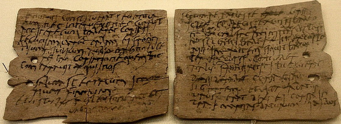 Two ancient wooden tablets covered with handwritten text in black ink, featuring faded and weathered cursive writing. The tablets are slightly worn and show holes on the left side, suggesting they were once bound together.