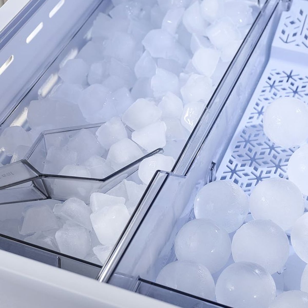 Close-up of an ice maker showing two compartments: one filled with square ice cubes and a scoop, the other containing round ice balls on a patterned tray.