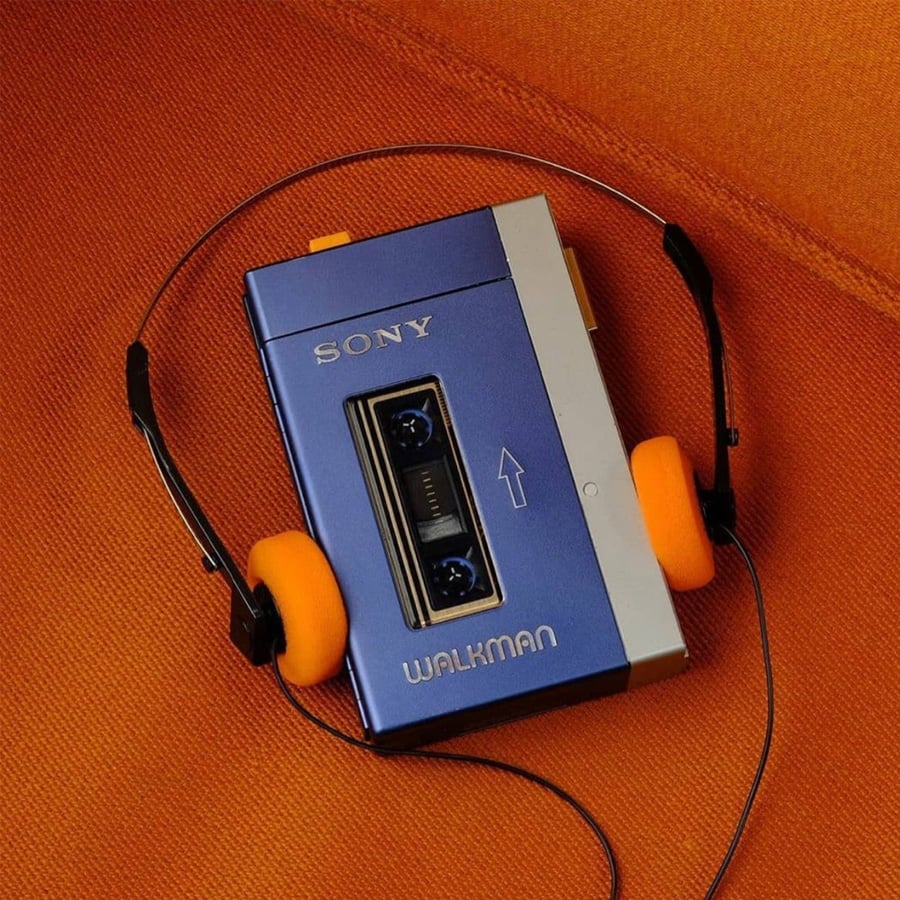 A blue Sony Walkman cassette player with orange foam headphones rests on an orange fabric surface.