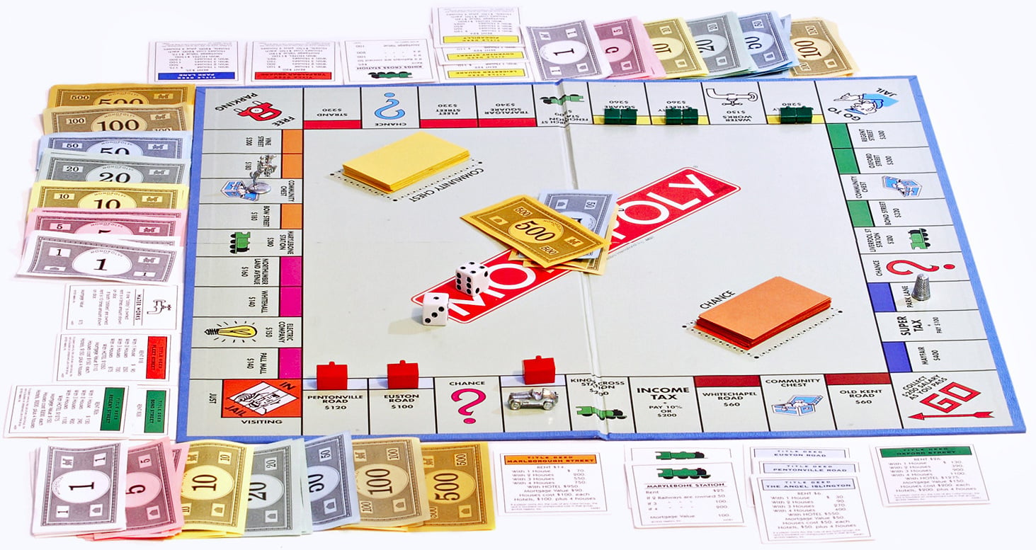 A Monopoly board game is set up with money, property cards, houses, hotels, dice, and Chance and Community Chest cards arranged around the board. The board displays spaces for properties, taxes, and corner squares.