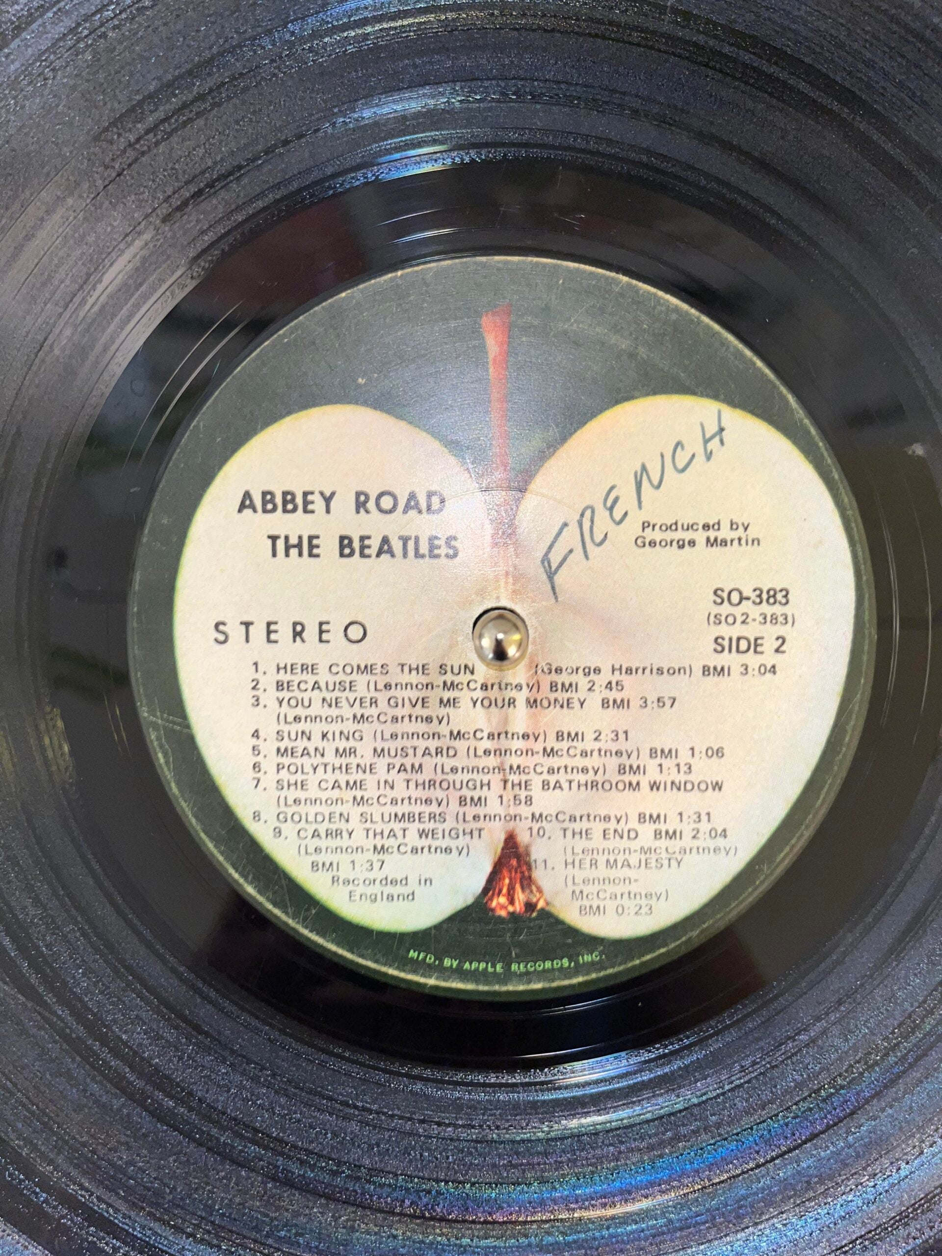 A close-up of The Beatles' "Abbey Road" vinyl record label, Side 2, listing songs and credits. The word "FRENCH" is handwritten in blue ink across the center of the label.