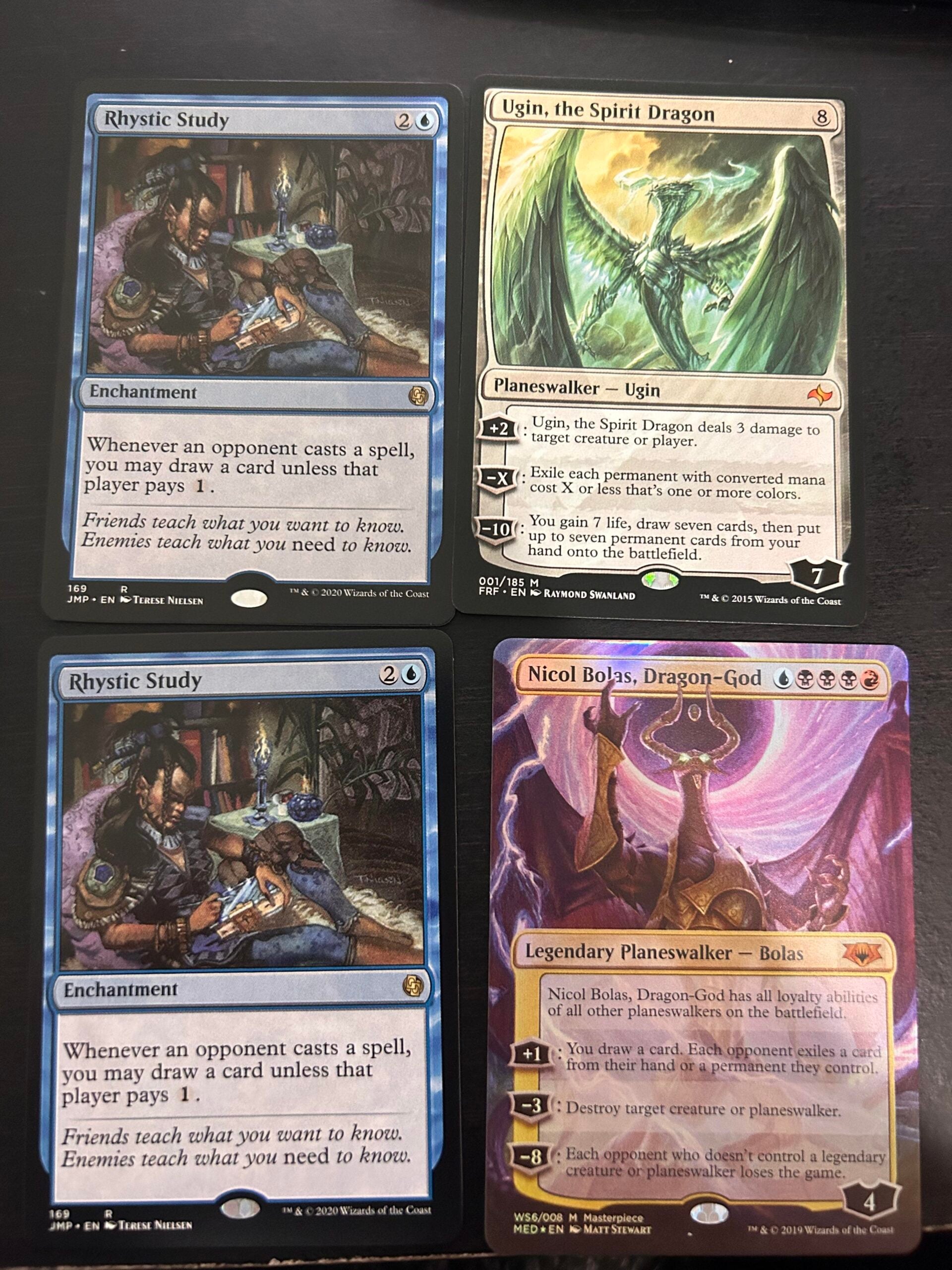 Four Magic: The Gathering cards on a table: two Rhystic Study cards (blue enchantment), Ugin, the Spirit Dragon (colorless planeswalker), and Nicol Bolas, Dragon-God (multicolored planeswalker).