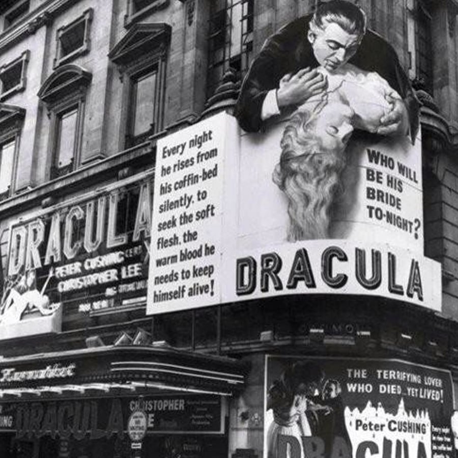 A black-and-white photo of a theater showing "Dracula," with a large poster of Dracula biting a woman's neck and dramatic text beside it. The marquee lists actors Peter Cushing and Christopher Lee.