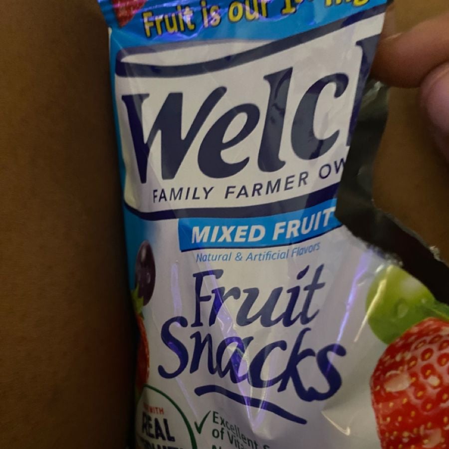A close-up of a Welch's Mixed Fruit Fruit Snacks package being held, with the package partially opened. The package displays images of fruit and the text "Fruit Snacks" clearly visible.
