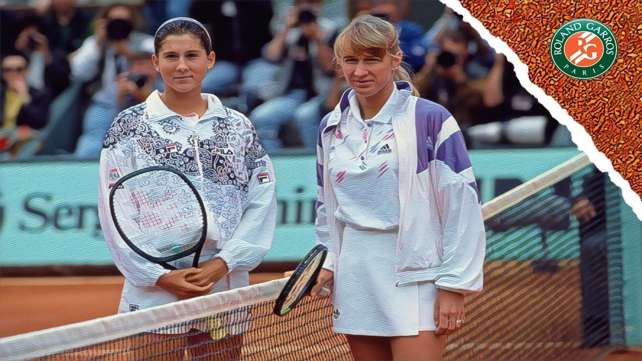 Two female tennis players stand at the net on a clay court, each holding a racket, with spectators in the background and a Roland-Garros logo in the top right corner.