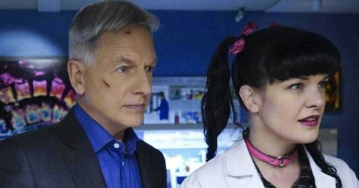 A man with gray hair and a facial scratch stands beside a woman with black hair in pigtails, wearing a white lab coat and pink choker, in a brightly lit laboratory setting.
