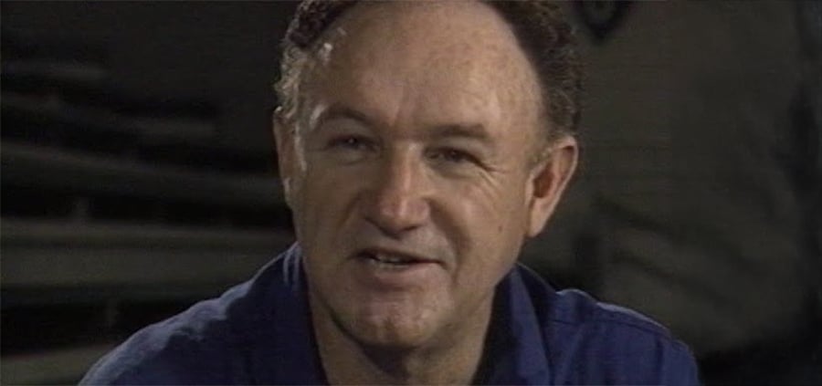 A middle-aged man with thinning hair and a slight smile looks past the camera, wearing a blue collared shirt in a dimly lit setting.