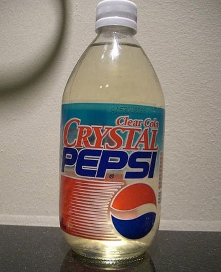 A clear plastic bottle of Crystal Pepsi, featuring a red, white, and blue label with the Pepsi logo and the words "Clear Cola Crystal Pepsi." The bottle is placed on a dark surface against a light background.