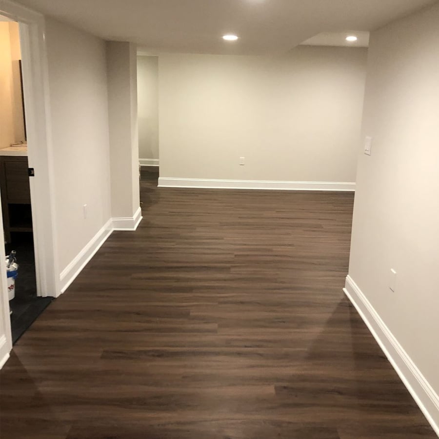 A basement with recessed lighting, white walls, white trim, and dark wood flooring. The space is empty, with doorways visible on the left and a small alcove at the back.