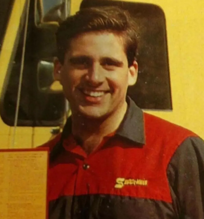 A smiling man wearing a red and black uniform with a yellow "S" logo stands in front of a yellow vehicle.
