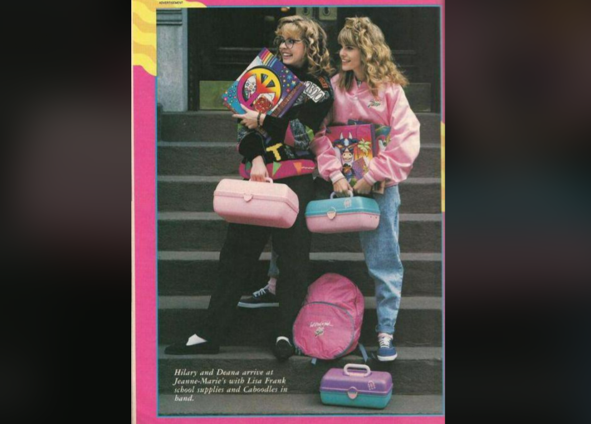 Two girls with curly hair stand on steps, smiling. They wear colorful sweaters, jeans, and sneakers, and each holds a plastic caboodle case and Lisa Frank school supplies. A pink backpack sits at their feet.