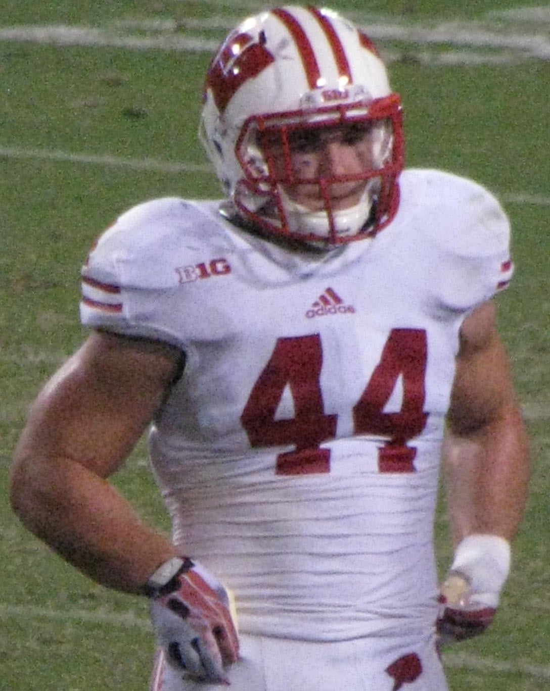A football player wearing a white uniform with red accents and the number 44 on the front stands on a field. He has a red and white helmet and appears to be from a college team.